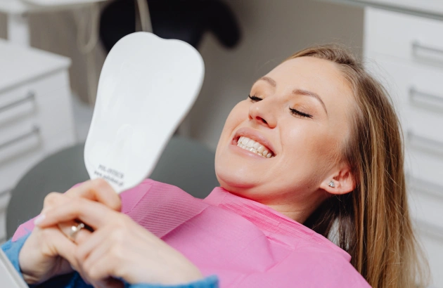 Woman examining teeth in dental mirror at dentist office wearing pink shirt